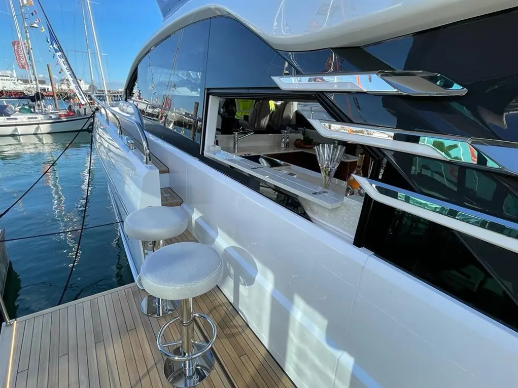 Stylish yacht deck with two bar stools, a drinks counter, and reflections on the water, showcasing a luxury boating experience.